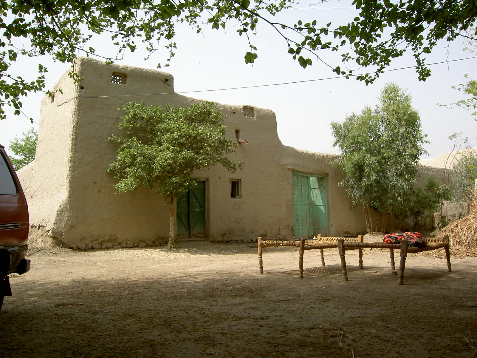 A traditional village home in Punjab, Pakistan, with trees and charpais in its courtyard